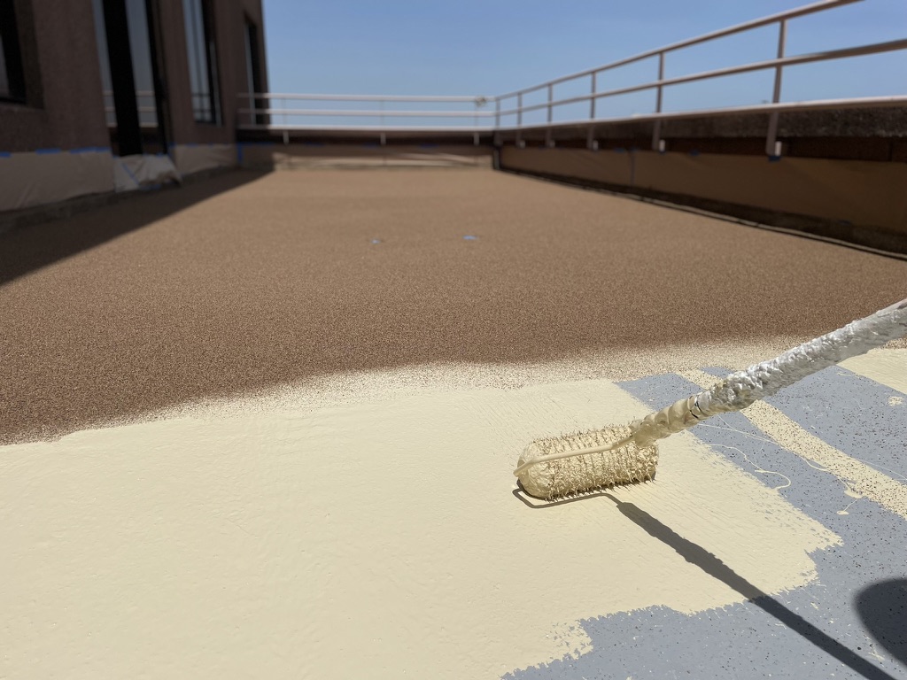 Tan silicone coating with ceramic granules being applied to a Skymark Tower balcony deck