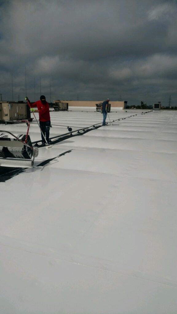 Crew roller-applying white silicone roof coating at Cedar Hill Crossing, Cedar Hill, Texas