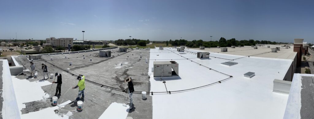 Wide view of a commercial roof restoration in progress, bright white coating advancing across the deck