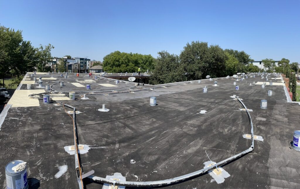 Existing bitumen roof at Monarch St before coating, showing years of accumulated patchwork across the deck