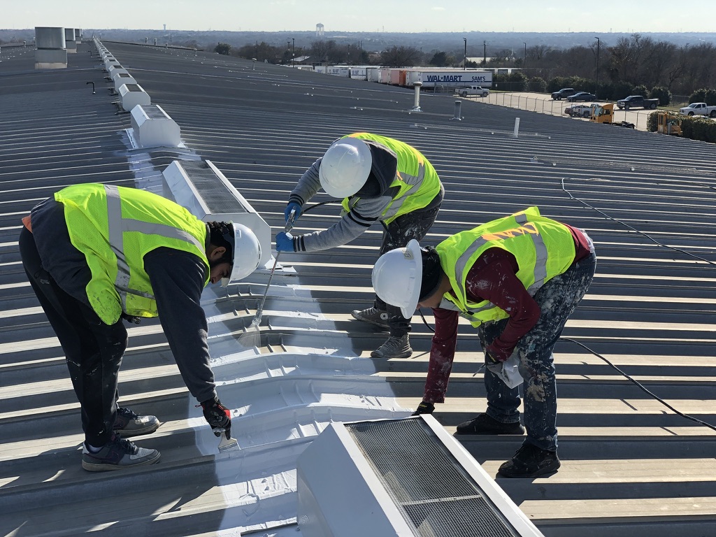 Crew brush-applying elastomeric coating to roof seams and vents at the DeSoto Walmart Distribution Center