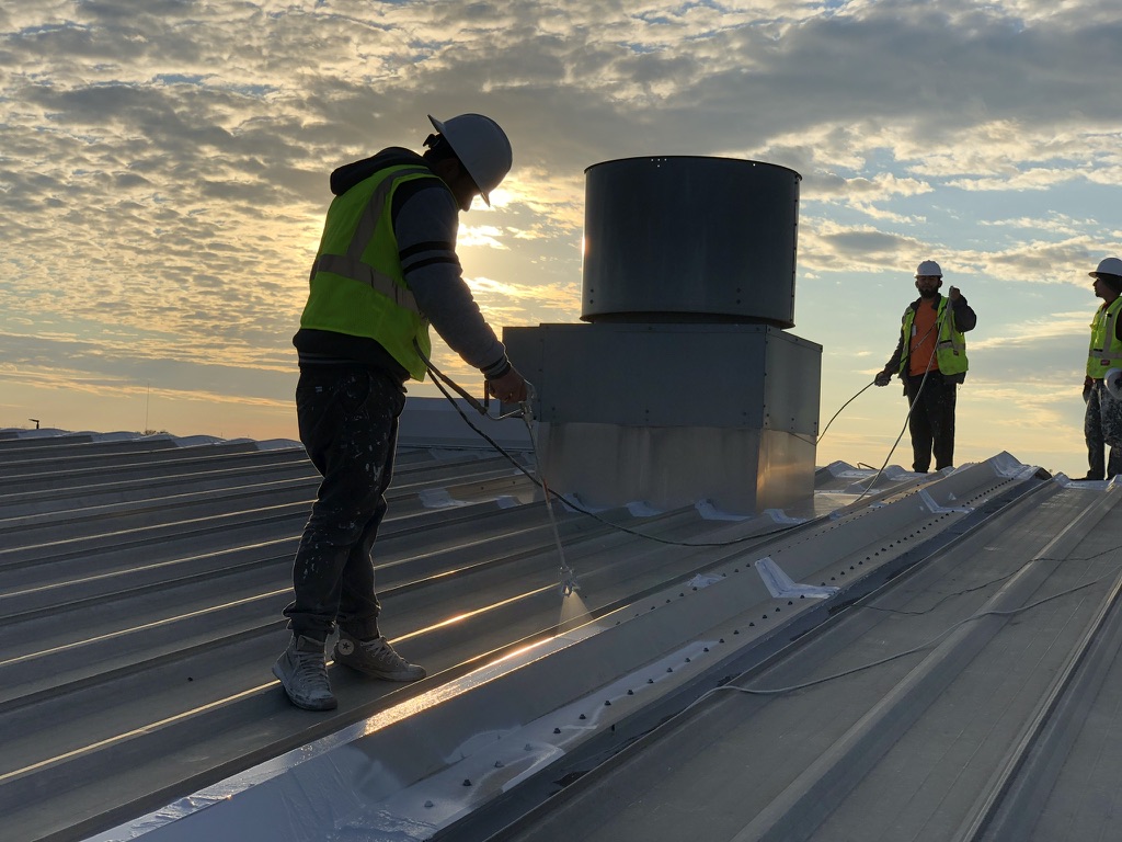 Spray application of acrylic roof coating along a metal roof ridge in DeSoto, Texas