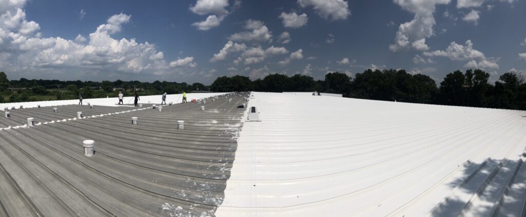Large industrial metal roof mid-restoration showing the coated white section meeting the bare metal panels