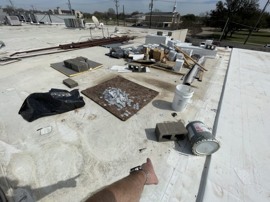 Leftover materials, trash, and loose fastener plates left on the strip center roof at 310 N Central Expressway, McKinney
