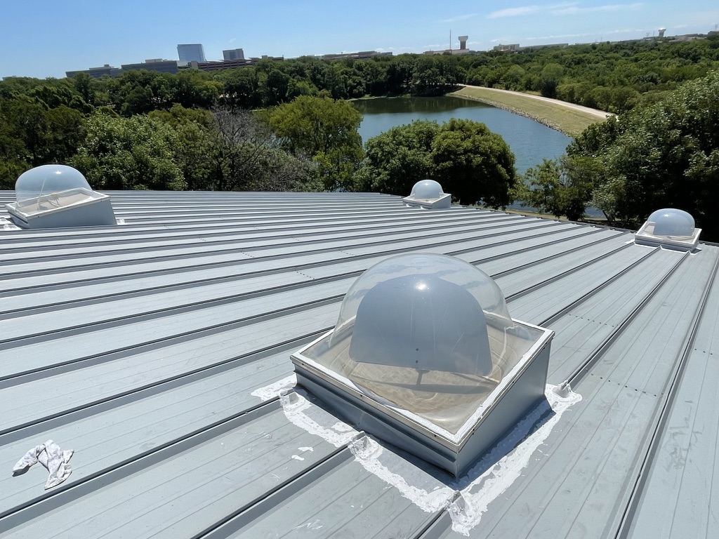 Silicone roof coating applied around the skylight curb and metal roof transition in Plano, Texas