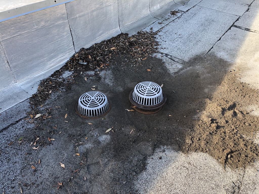 Failed commercial roof drain on Modified Bitumen roofing system before silicone repair at AT&T, 211 McKinney Ave, Princeton, TX