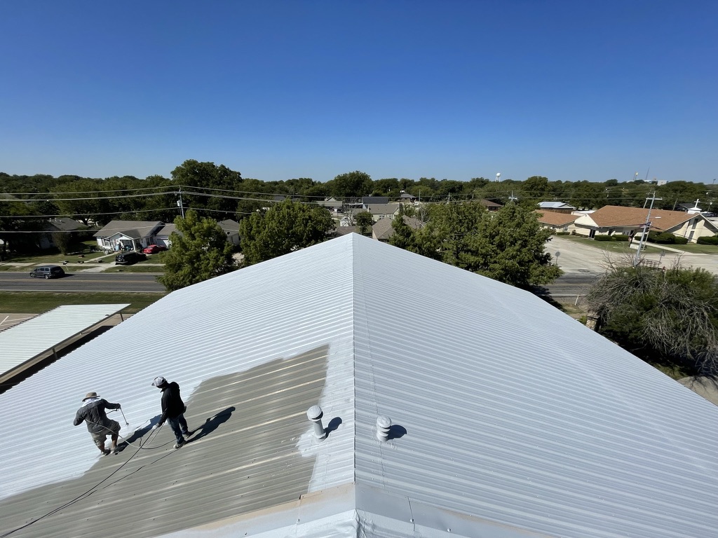 Spray application of dark grey acrylic roof coating on R-panel roof in Sanger, TX