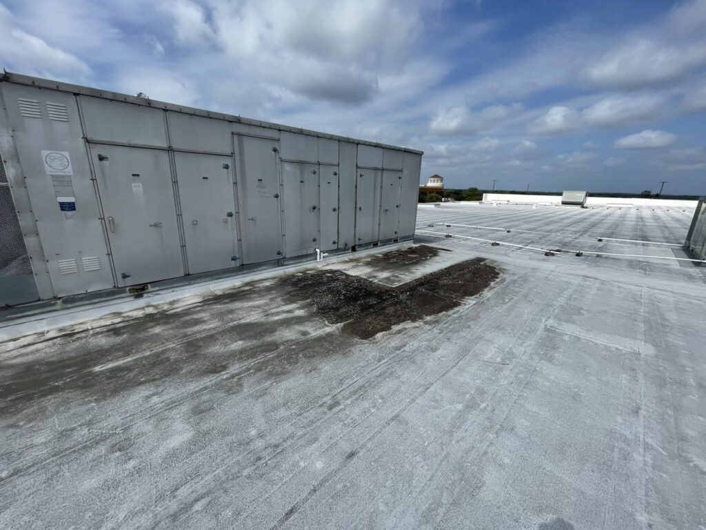 Coating delamination tracing the path of dripping water toward the gutters on the Arlington commercial roof