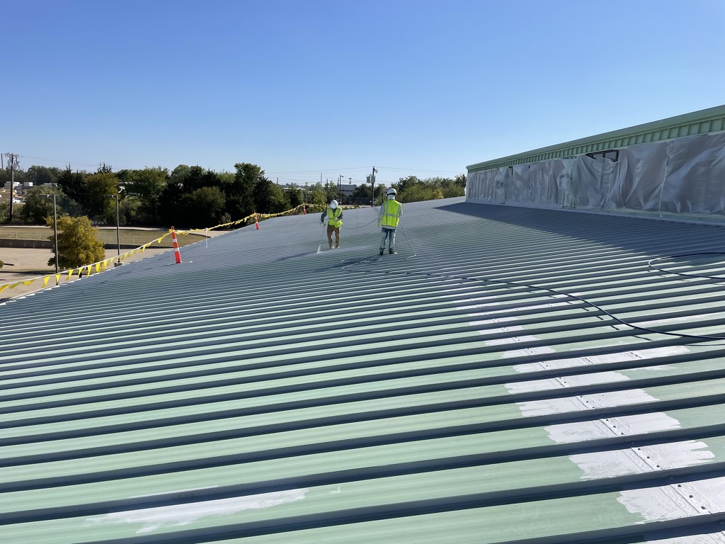 Charcoal acrylic coating advancing across the standing seam panels in Irving, TX