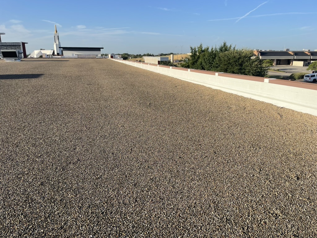 Gravel reset over the finished silicone coating at the base of the parapet wall, Storage Sense, Irving, TX