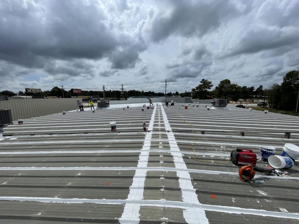 Silicone roof coating application in progress, gray metal roof transitioning to white, Conroe, TX