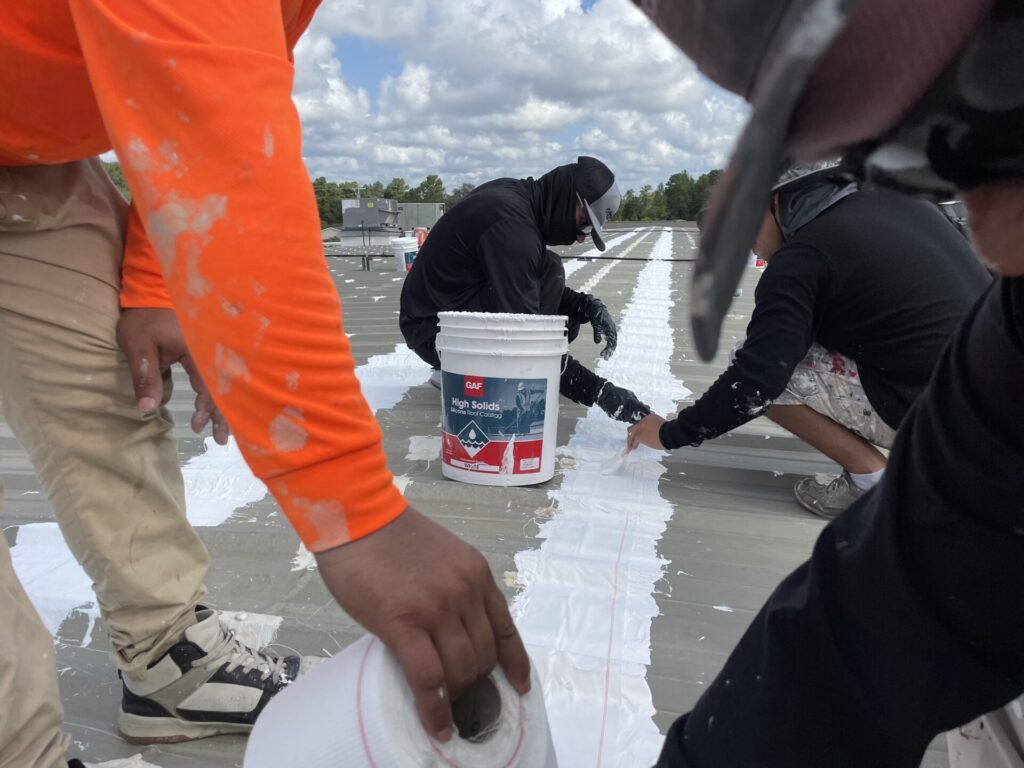 Crew applying GAF High Solids Silicone seam coating with reinforcing fabric over an R-panel seam, Conroe, TX