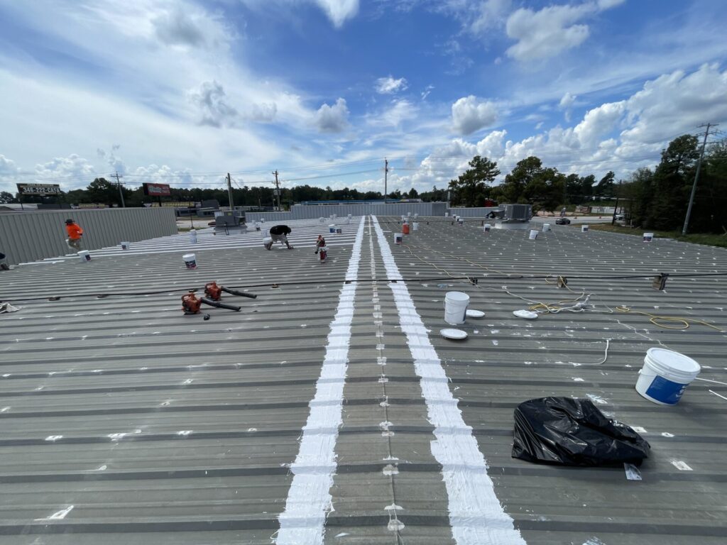 Crew applying 3-course silicone seam treatment across the horizontal seams of the metal roof, Conroe, TX