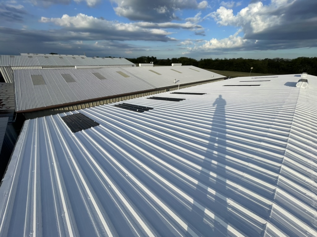 Finished white coating across metal roof ribs and around a penetration in McKinney