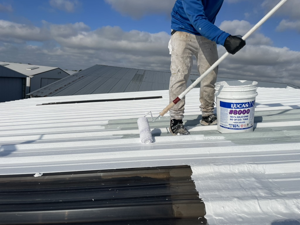 Roller application beside a Lucas 8000 silicone coating pail on the McKinney metal roof